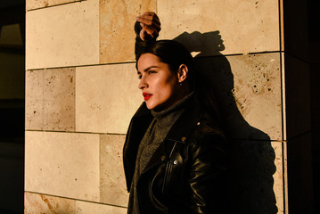 Young beautiful brunette girl posing at sunset on a wall background on a city street