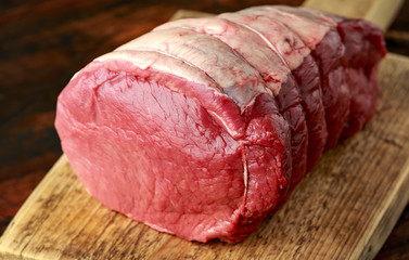 butcher slicing Fresh Raw top side beef meat on rustic wooden chopping board
