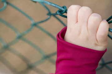 A caucasian child holding her right hand on the fence what is on the other side of it