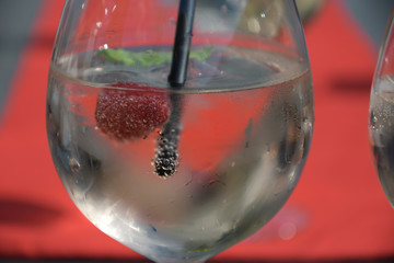 glas mit lillet sekt und himbeere und schwarzem strohhalm vor rotem hintergrund getränk bar