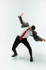 Young caucasian man moving flexible on white studio background. Male model in office attire bending...