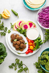Fresh homemade falafels served with tahini sauce, herbs and vegetables, top down view