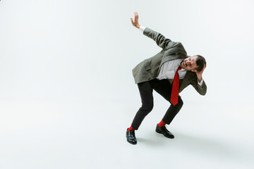 Young caucasian man moving flexible on white studio background. Male model in office attire bending...