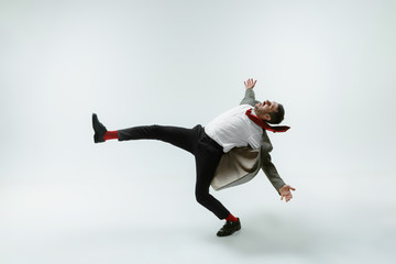 Young caucasian man moving flexible on white studio background. Male model in office attire bending over, avoiding something, catched in motion and action. Looks angry, scared, fighting. Emotions.