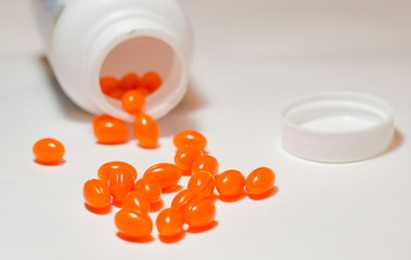 Capsules of orange color poured out of the jar on a white background. Vitamins, Sports nutrition. Close-up, selective focus.