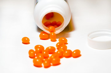 Capsules of orange color poured out of the jar on a white background. Vitamins, Sports nutrition....