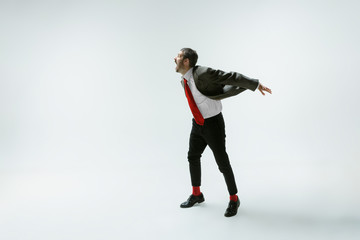 Young caucasian man moving flexible on white studio background. Male model in office attire bending...