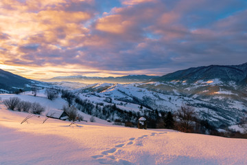 mountainous countryside in winter at sunrise. snow covered hills and fields of carpathian rural area rolling off in to the distant krasna ridge. glowing fog in the valley. colorful clouds on the sky