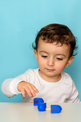 Jewish curly haie sweet little boy playing with blue color dreidel at home.