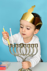 Kid celebrating Hanukkah Israel holiday. Little jewish boy puts candles on traditional menorah.