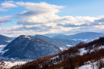 mountainous rural landscape on a sunny winter day. snow covered fields on hills. village in the distant valley. landscape with clouds on the sky