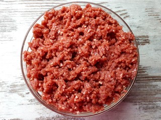  Close-up of raw, freshly prepared minced meat from animal meat in a glass bowl on a wooden surface