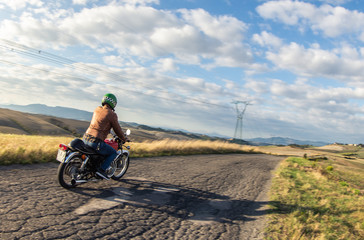 Man riding motorbike along a country road on tuscan hills landscape at sunset. Tuscany, Italy.