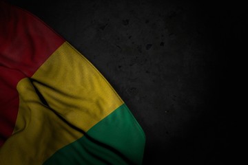 Fototapeta na wymiar beautiful dark image of Guinea flag with large folds on black stone with free space for your text - any celebration flag 3d illustration..