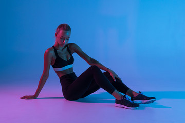 Full length portrait of attractive woman wearing black tracksuit doing gymnastic sitting on the floor isolated over purple background - obrazy, fototapety, plakaty