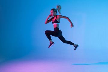 Sporty young woman fitness jumping isolated on purple light background - obrazy, fototapety, plakaty
