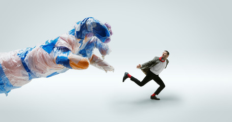 Young caucasian man avoiding big plastic hand on white studio background. Male model in office attire fighting in motion and action. Looks angry, scared, pressured. Eco problems, pollution, recycling.