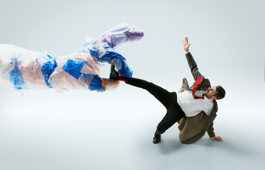 Young caucasian man avoiding big plastic hand on white studio background. Male model in office...