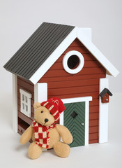 Kleiner Bär mit Weihnachtsmannmütze vor kleinem Haus