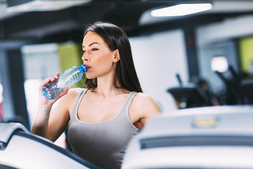 Fototapeta na wymiar Girl drinking water in gym after workout.