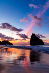 Stunning colorful sunset in Cacimba do Padre beach in Fernando de Noronha, Brazil with water reflection. Several clouds turned pink forming colorful rays in the sky and in the sand.
