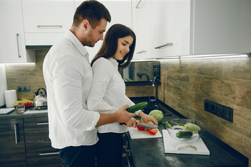 Lovely couple at home in a kithen. Woman and man prepare salad. Woman in a white shirt