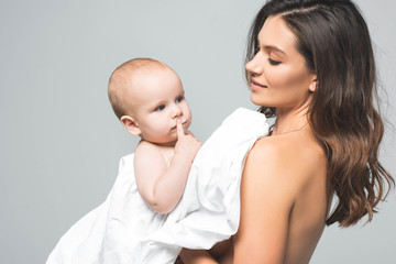portrait of attractive smiling naked mother hugging baby boy, isolated on grey