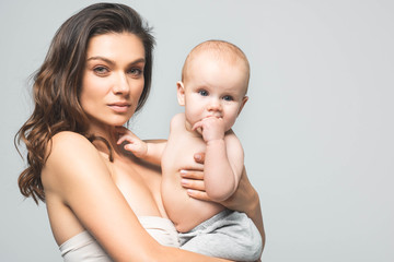 portrait of beautiful mother holding baby boy, isolated on grey
