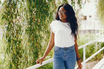 Cute black girl in a park. Lady in a white t-shirt and blue jeans. Woman in a sunglasses