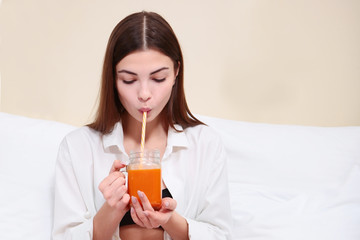 Beautiful girl drinking juice in bed. Breakfast concept at home or in the hotel.