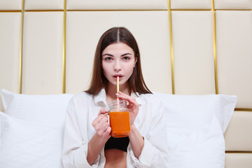 Beautiful girl drinking juice in bed. The concept of Breakfast at home or at the hotel. Copy space.
