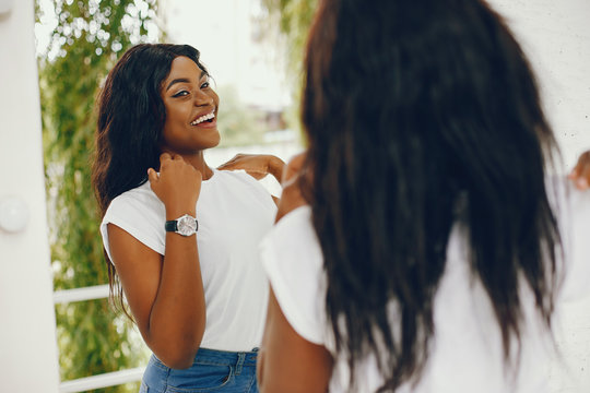 Cute black girl near white wall. Lady in a white t-shirt and blue jeans. Woman with watch