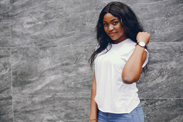 Cute black girl near gray wall. Lady in a white t-shirt and blue jeans.