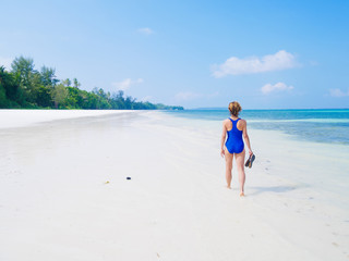 Woman walking on tropical beach. Rear view white sand beach turquoise trasparent water caribbean sea real people. Indonesia Kei Islands Moluccas travel destination.