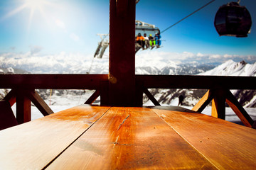 Wooden table background of free space and winter landscape of mountains.Ski time and blue sky with sun. 