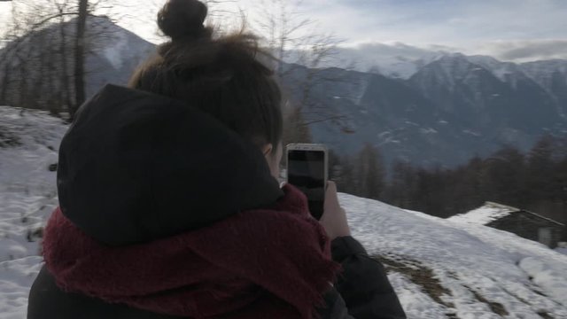 Girl taking a snapshot of a winter landscape in the mountains