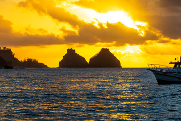Naklejka na ściany i meble Stunning sunset from a boat in Fernando de Noronha, Brazil. Morro Dois Irmãos (Two Brothers Mountain) can seen at distance.