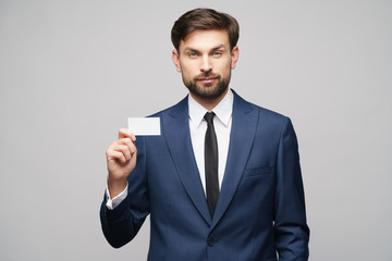 studio photo of young handsome businessman wearing suit holding business card