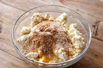 Raw mixture for making cottage cheese cakes in glass bowl on old wooden background