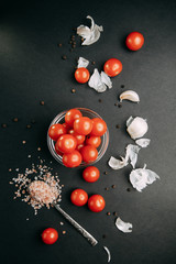 Ingredients on black background. Cherry tomatoes with garlic and salt in bowls.
