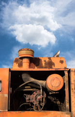 Diesel engine of an orange excavator on blue sky with clouds.