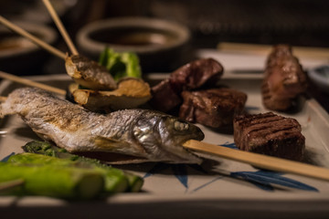 fish on a stick, served on a plate with an assortment of vegetables and steak
