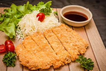 Japanese deep fried breaded pork cutlet served with shredded cabbage and tonkatsu sauce on wooden plate and black background. Stock photo