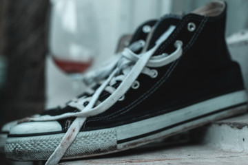 black sneakers with white laces on a white wood and a blurred glass of wine in the background