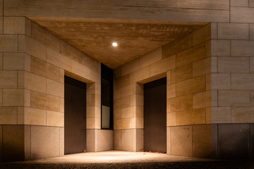 Two doors and a lamp in a triangular niche, two doors and sandstone facade at night, modern architecture