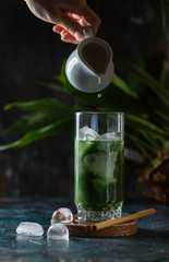 Cold Matcha green tea. Healthy eating concept. Pouring milk into a glass of green tea.