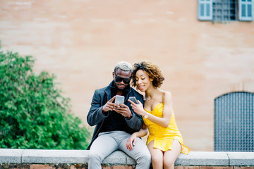 Smiling young man and smiling young woman using smart phone