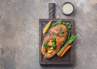 Fried salmon steak with vegetables on wooden board, copy space