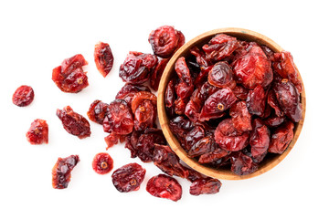 Dried cranberries in a wooden plate and scattered on a white background. The view of top.