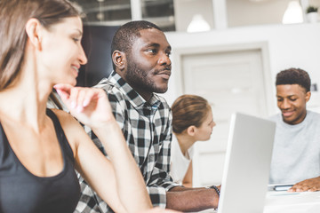 A team of young office workers, businessmen with laptop working at the table, communicating together in an office. Corporate businessteam and manager in a meeting. coworking.